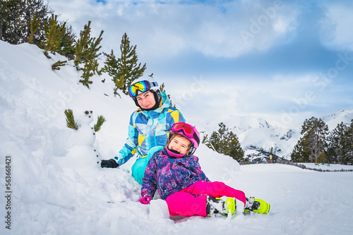 Family, mother and daughter, build a small snowman next to ski slope. Ski winter holidays in Andorra, El Tarter, Pyrenees Mountains