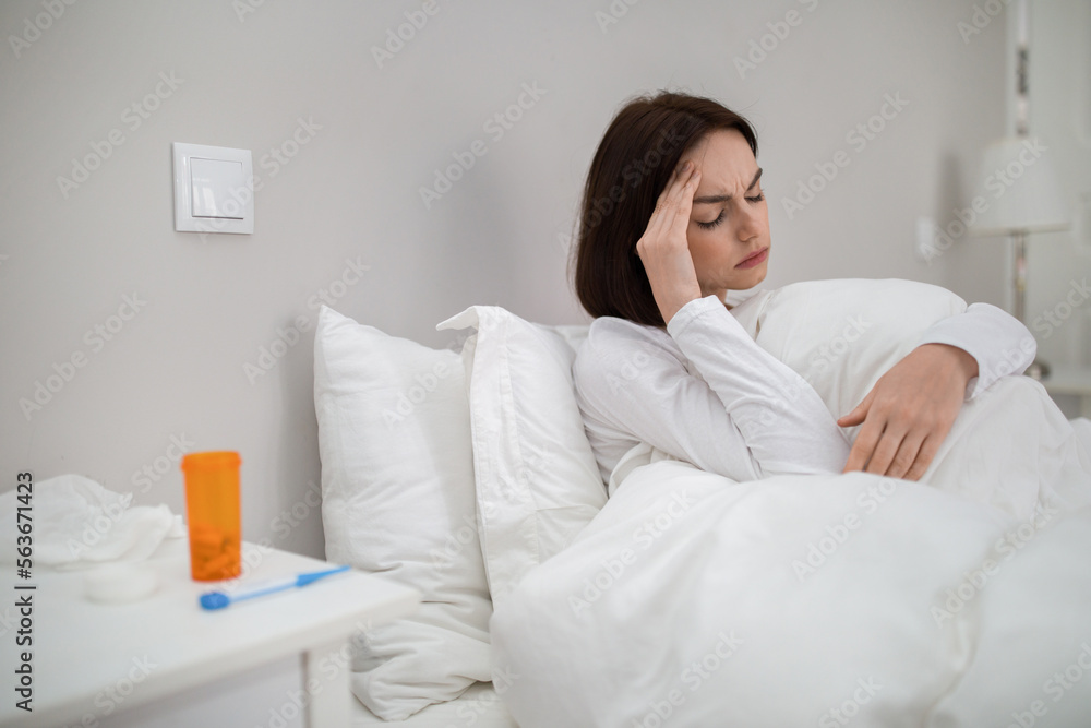 Sick woman with fever sitting in bed, touching head Sick woman with fever sitting in bed, touching head