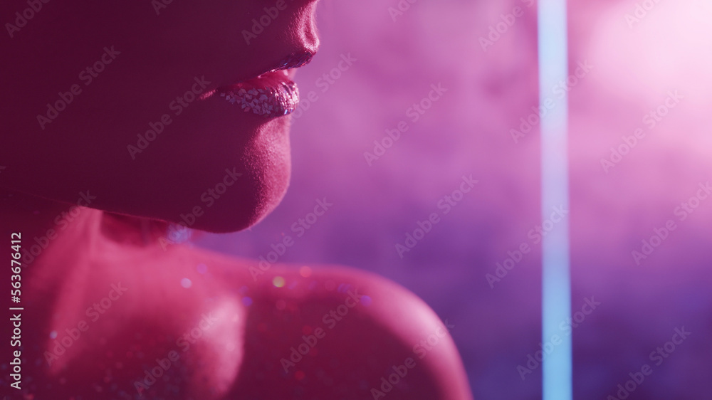 Fototapeta premium Neon beauty. Glitter skin. Nightclub look. Closeup of woman face with metallic lips sparkling bare shoulder on blur pink color light smoke free space background.
