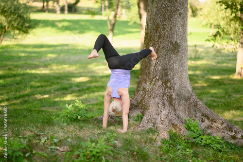 Middle-aged woman doing yoga, doing handstand exercises near a tree.Adho Mukha Vrikshasana.Concept of active lifestyle, body care, training, stretching, yoga.