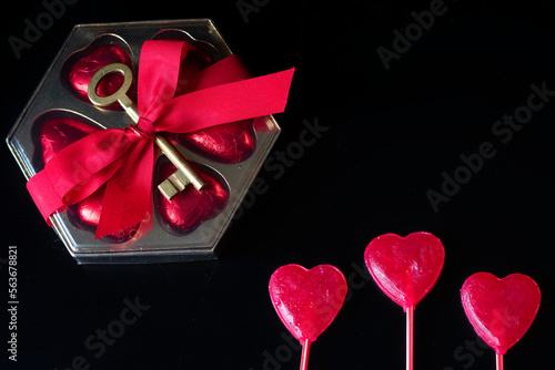 Present on a black background, heart-shaped bombomes with a red ribbon and an old key on them, on the side red heart-shaped lollipops adorn the background. background for valentine's day mother's day