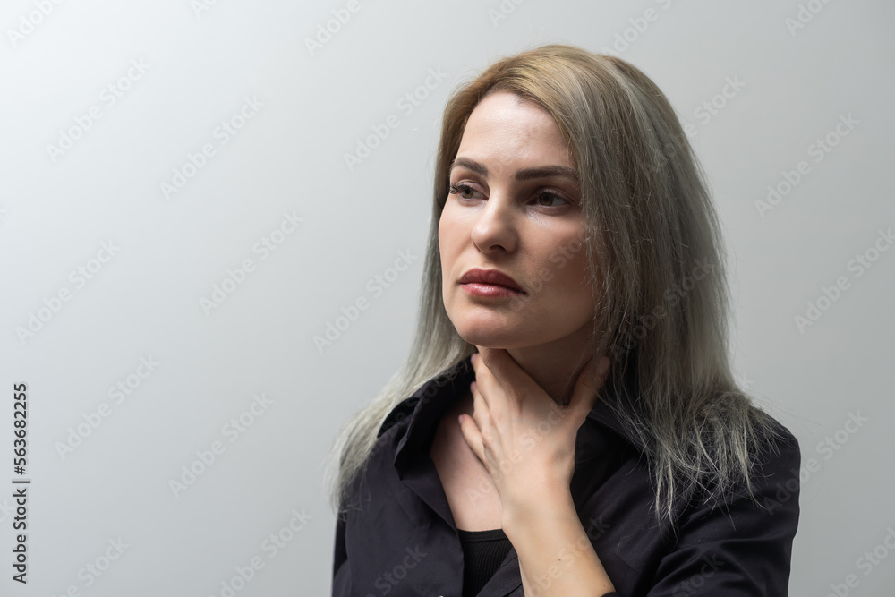 Closeup of sick woman having sore throat, tonsillitis, feeling sick, caught cold, suffering from painful swallowing, strong pain in throat, holding hand on her neck, isolated light background Closeup of sick woman having sore throat, tonsillitis, feeling sick, caught cold, suffering from painful swallowing, strong pain in throat, holding hand on her neck, isolated light background