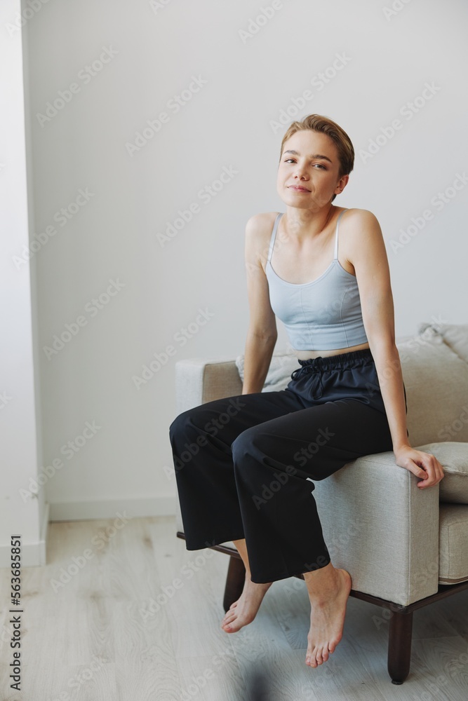 Teenage girl sitting on the couch at home smiling in home clothes and glasses with a short haircut, lifestyle without filters, free copy space Teenage girl sitting on the couch at home smiling in home clothes and glasses with a short haircut, lifestyle without filters, free copy space