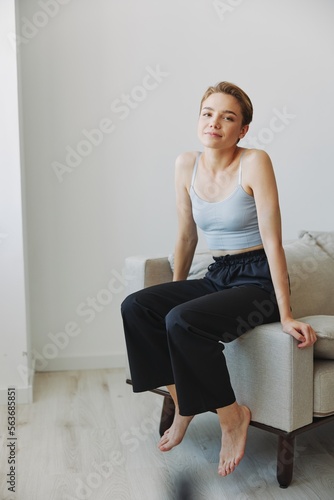 Teenage girl sitting on the couch at home smiling in home clothes and glasses with a short haircut, lifestyle without filters, free copy space