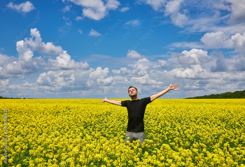 Man with arms outstretched. Handsome young man standing in a field of blooming yellow rapeseed flowers.