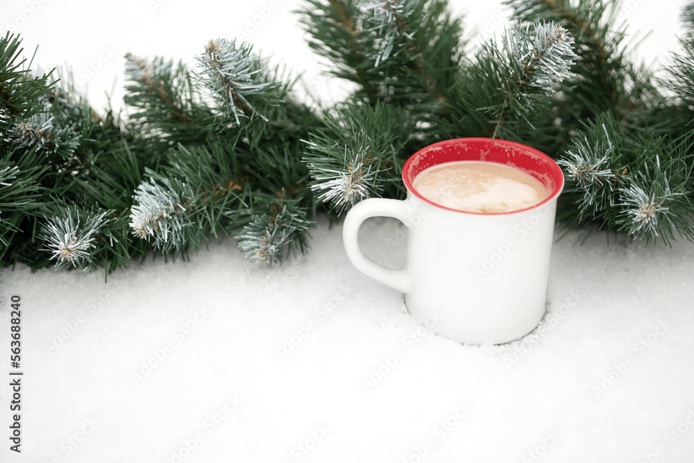 a mug of coffee on the snow near a coniferous garland.