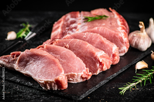 Chopped raw pork on a stone board with rosemary and garlic.