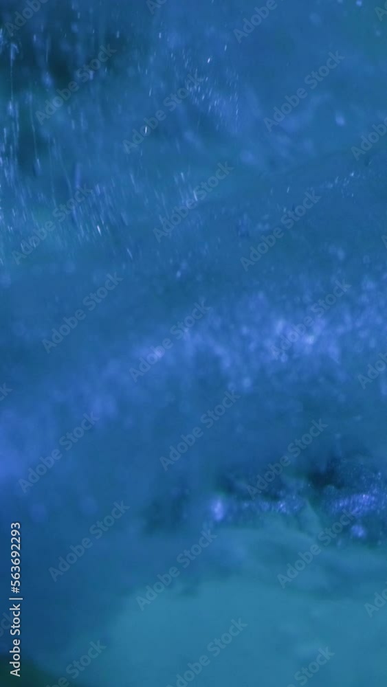Vertical video. Glitter splash. Ink water. Ice flakes. Defocused blue color paint drop mist flow motion on frost ice texture surface abstract background. Vertical video. Glitter splash. Ink water. Ice flakes. Defocused blue color paint drop mist flow motion on frost ice texture surface abstract background.