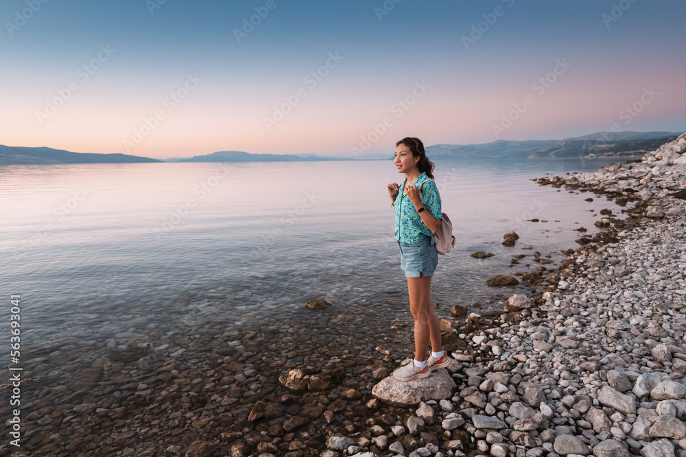 Happy girl traveling and enjoying the view of the lake or sea coast on a pebble beach. Egirdir lake, Turkiye