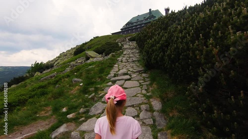 Little girl climbing on the top of the mountain Szrenica, Szklarska Poręba, Poland overlooking the mountain hut, on a foggy summer day