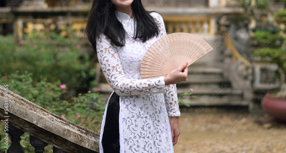 Naklejka premium Vietnamese woman in traditional dress Ao Dai, holding a wooden fan