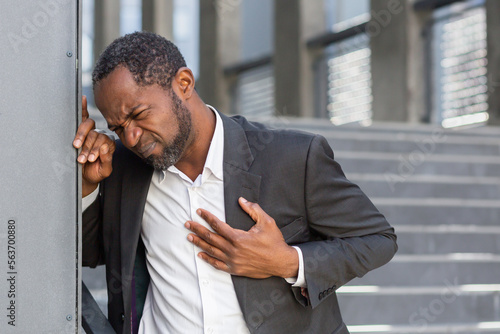 Принти на полотні Heart attack, African American man has severe chest pain, businessman outside office building on stairs writhing in chest pain