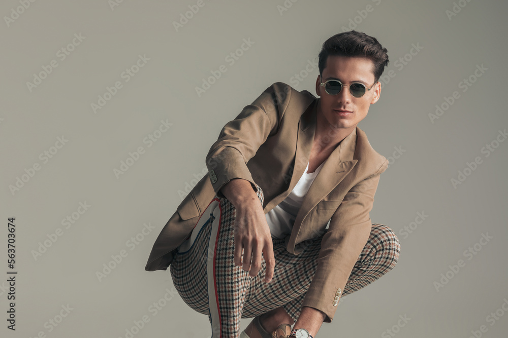 happy man with sunglasses wearing beige jacket and plaid pants and crouching happy man with sunglasses wearing beige jacket and plaid pants and crouching