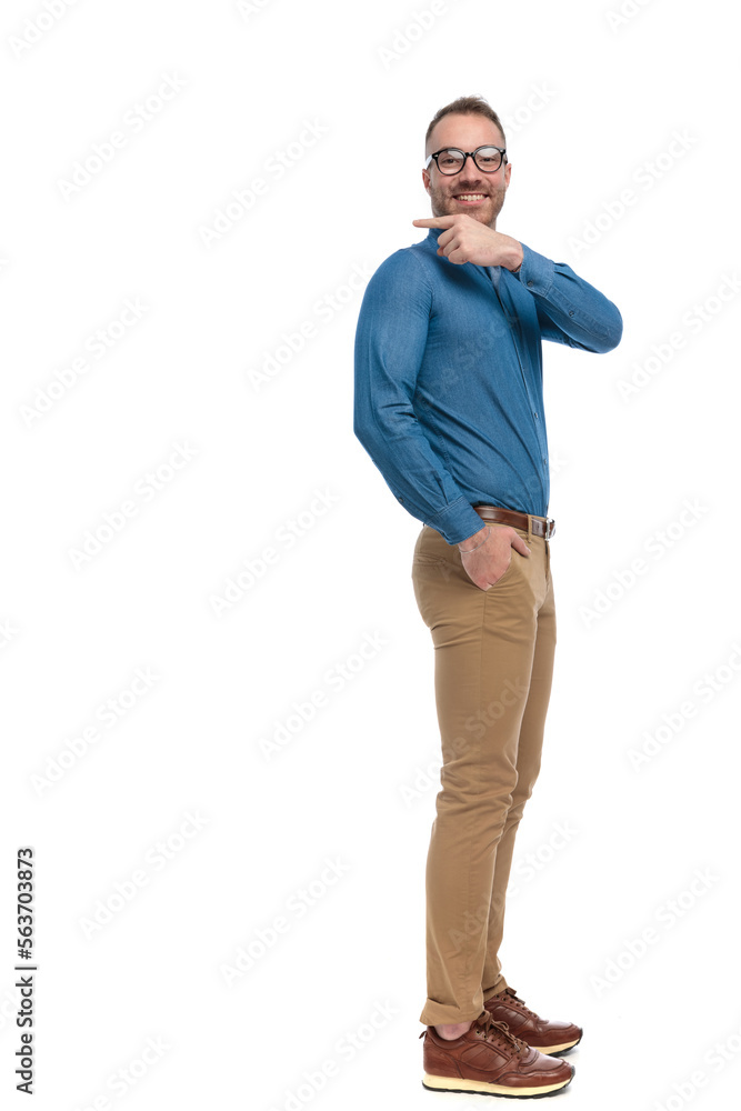 side view of happy young man in denim shirt pointing finger behind side view of happy young man in denim shirt pointing finger behind