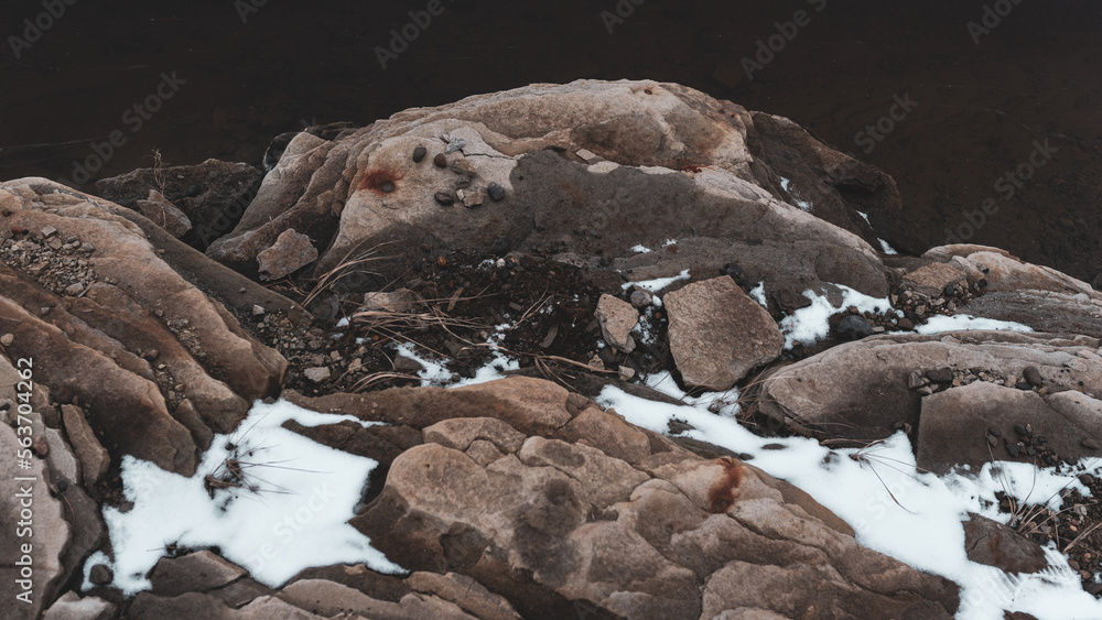 Photo of a rock outcrop on the shore with dark water with snow.