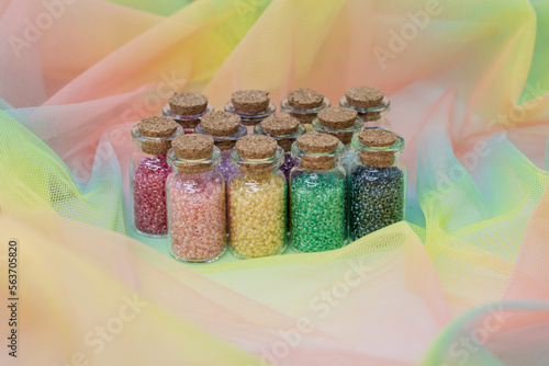 Multicolored beads in glass jars with cork isolated on a colored background.