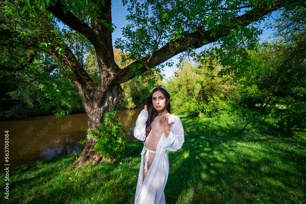 A girl in a bathing suit and a white cape near a broken tree among greenery. A girl in a bathing suit and a white cape near a broken tree among greenery.