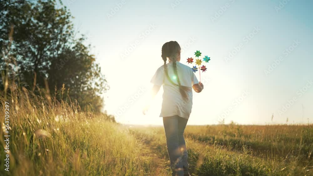 Happy child runs in park with toy turbine. Windy toy in hands of girl in nature. Child runs in the summer on green grass. Toy turbine in the wind in the park. Summer walk on vacation girls at sunset Happy child runs in park with toy turbine. Windy toy in hands of girl in nature. Child runs in the summer on green grass. Toy turbine in the wind in the park. Summer walk on vacation girls at sunset