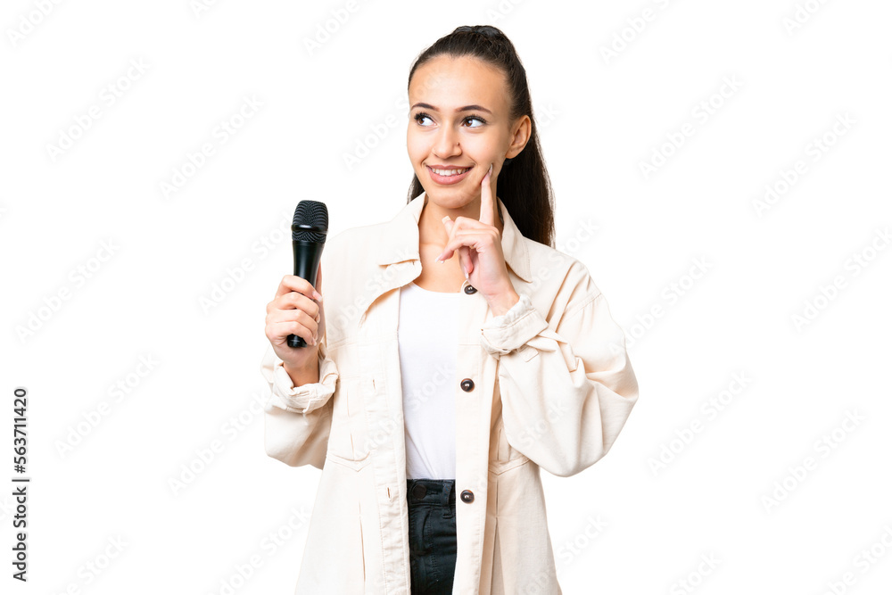 Young singer woman picking up a microphone over isolated chroma key background thinking an idea while looking up Young singer woman picking up a microphone over isolated chroma key background thinking an idea while looking up