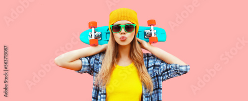 Portrait of stylish blonde young woman model with skateboard wearing colorful yellow hat on pink background