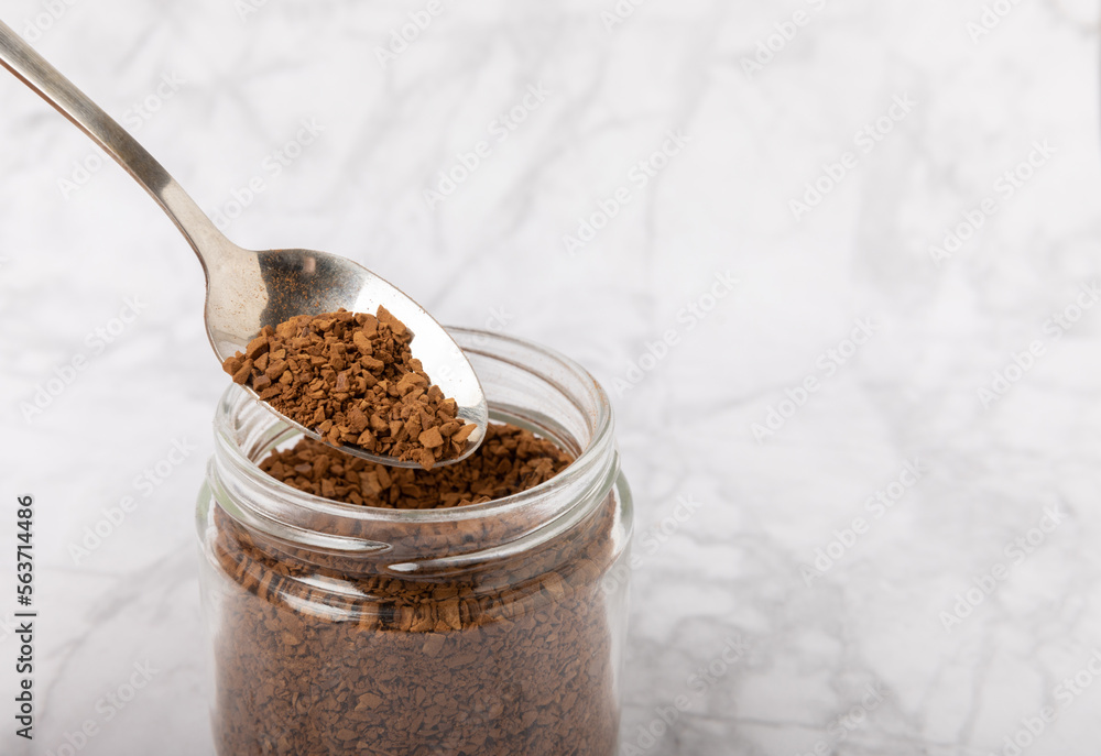 Instant coffee in a spoon and a glass jar on a white marble background. Place for text. Space for copy text Instant coffee in a spoon and a glass jar on a white marble background. Place for text. Space for copy text