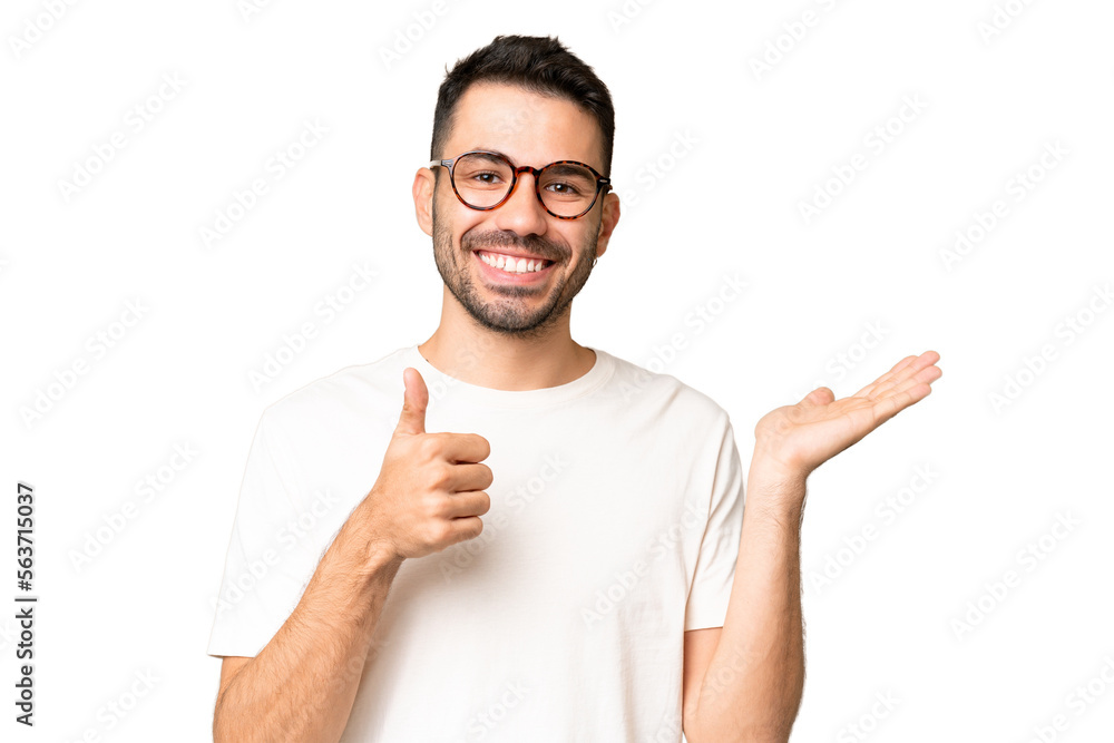 Young handsome caucasian man over isolated chroma key background holding copyspace imaginary on the palm to insert an ad and with thumbs up
