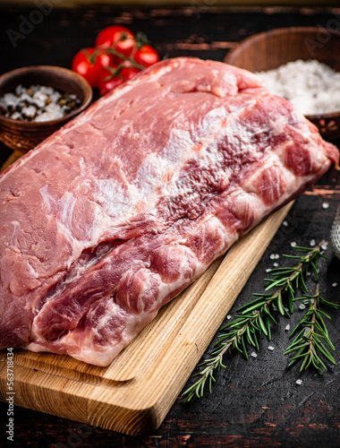 A piece of raw pork on a cutting board with tomatoes, spices and rosemary.