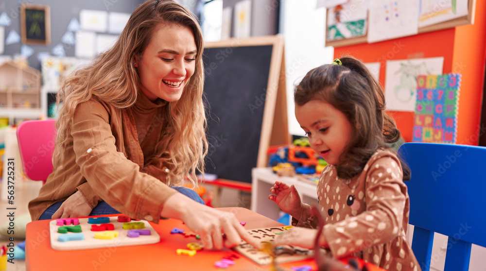 Teacher and toddler playing with maths puzzle game sitting on table at kindergarten Teacher and toddler playing with maths puzzle game sitting on table at kindergarten