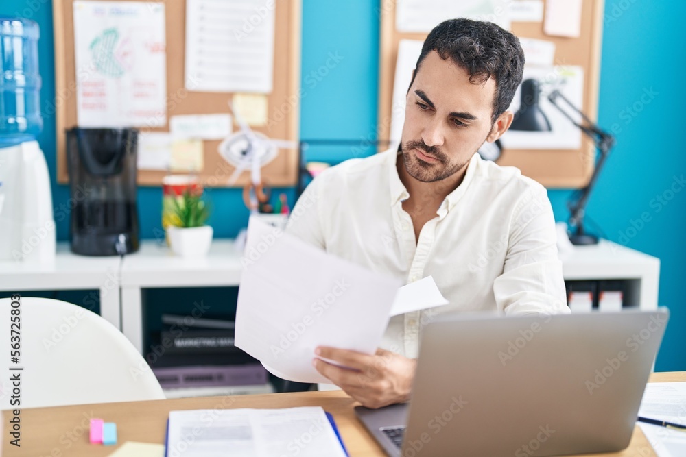 Young hispanic man business worker using laptop reading document at office Young hispanic man business worker using laptop reading document at office