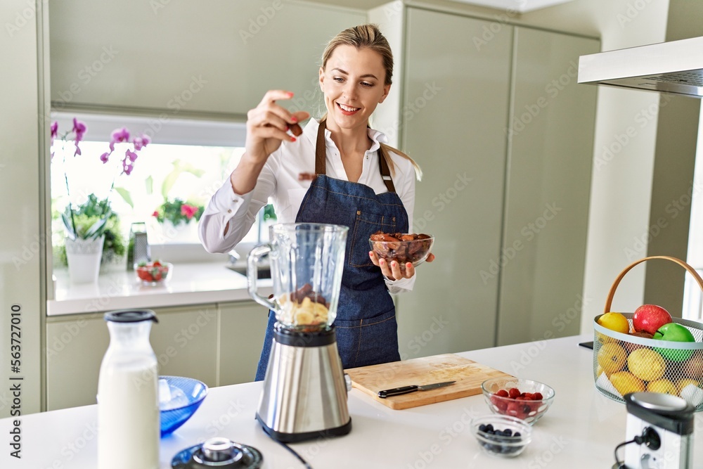 Young blonde woman smiling confident pouring dates on blender at kitchen Young blonde woman smiling confident pouring dates on blender at kitchen