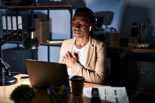 Beautiful black woman working at the office at night smiling with hands on chest with closed eyes and grateful gesture on face. health concept.