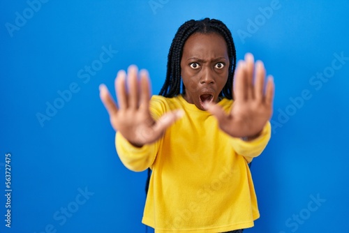 Beautiful black woman standing over blue background doing stop gesture with hands palms, angry and frustration expression