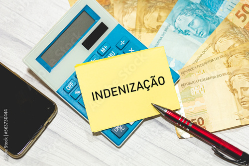 A palavra Indenização escrita em um pedaço de papel que está sobre uma calculadora. Notas do Real Brasileiro na composição. Economia brasileira. photo