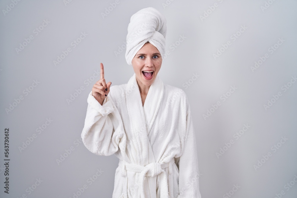 Blonde caucasian woman wearing bathrobe pointing finger up with successful idea. exited and happy. number one.