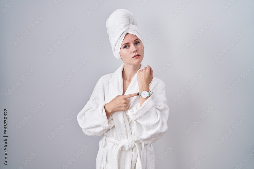 Blonde caucasian woman wearing bathrobe in hurry pointing to watch time, impatience, looking at the camera with relaxed expression - obrazy, fototapety, plakaty 