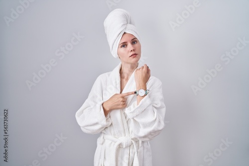 Blonde caucasian woman wearing bathrobe in hurry pointing to watch time, impatience, looking at the camera with relaxed expression photo