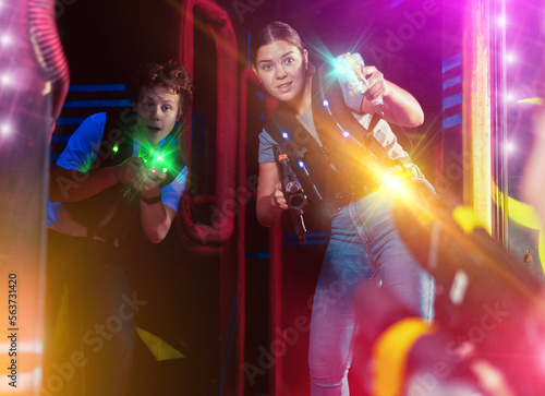 Two exciting players guy and woman with laser weapons in dark laser tag room