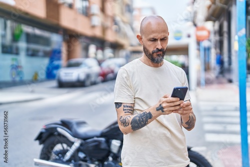 Young bald man using smartphone with serious expression at street
