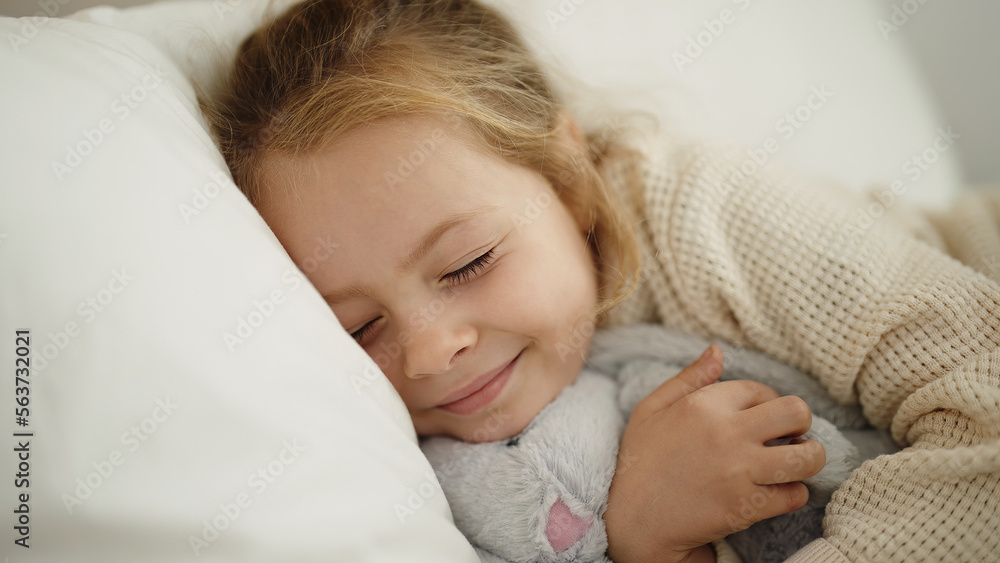 Adorable blonde girl hugging rabbit doll lying on bed at bedroom Adorable blonde girl hugging rabbit doll lying on bed at bedroom