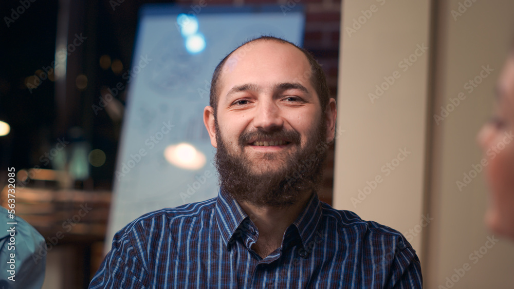 Obraz premium Employee looking at camera in business meeting, smiling, coworkers talking in boardroom, slow motion. Colleagues brainstorming, company worker in coworking space portrait close up. Handheld shot.