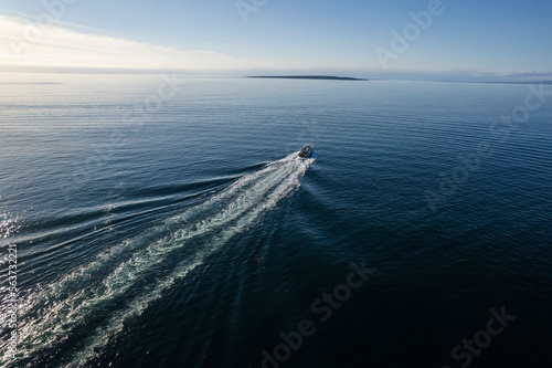 Small ferry boat in blue ocean on the way to Aran island, Ireland. Wake behind cruise ship. Warm sunny day with clear blue sky. Travel and transportation industry. Popular route from Doolin port. © mark_gusev