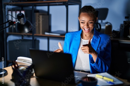 Beautiful african american woman working at the office at night pointing fingers to camera with happy and funny face. good energy and vibes.