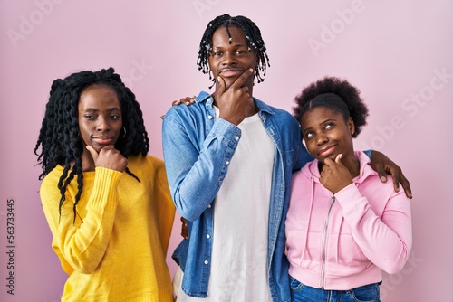 Group of three young black people standing together over pink background looking confident at the camera smiling with crossed arms and hand raised on chin. thinking positive. © Krakenimages.com