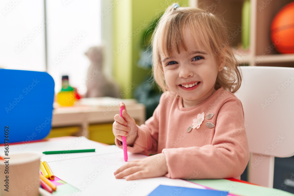 Adorable blonde girl preschool student sitting on table drawing on paper at kindergarten Adorable blonde girl preschool student sitting on table drawing on paper at kindergarten