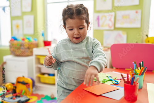 Adorable hispanic toddler student drawing on paper standing at kindergarten