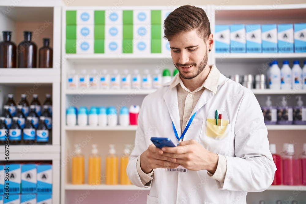 Young caucasian man pharmacist using smartphone working at pharmacy
