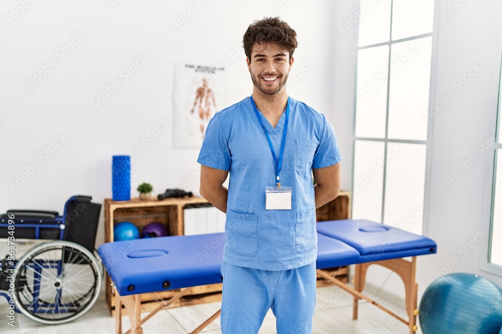Young hispanic man wearing physio therapist uniform standing at clinic Young hispanic man wearing physio therapist uniform standing at clinic