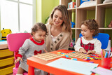 Teacher with girls playing with maths puzzle game sitting on table at kindergarten