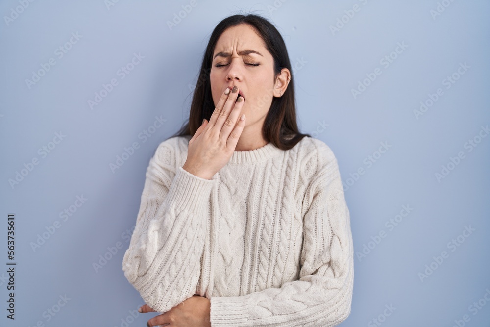 Young brunette woman standing over blue background bored yawning tired covering mouth with hand. restless and sleepiness. Young brunette woman standing over blue background bored yawning tired covering mouth with hand. restless and sleepiness.