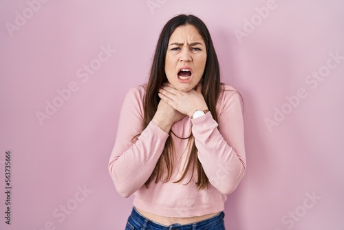 Young brunette woman standing over pink background shouting suffocate because painful strangle. health problem. asphyxiate and suicide concept.